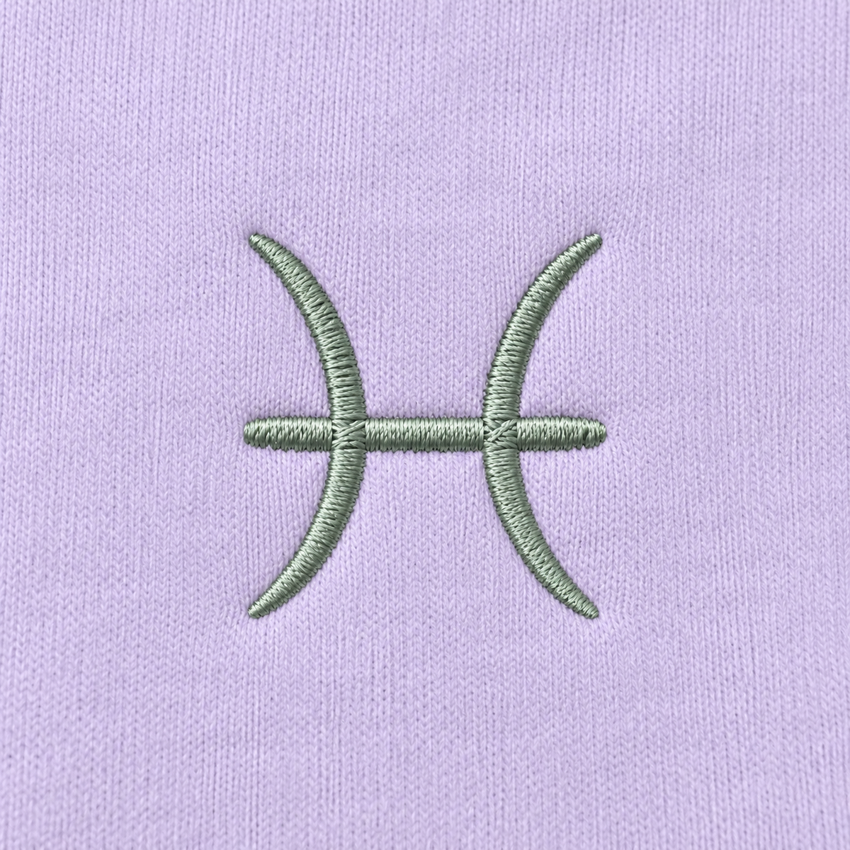 Close-up of embroidered Pisces zodiac glyph on light lavender hoodie fabric of Gamla Healing